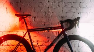 A bike against a whitewashed brick wall with bright red lights on at the back and a bright white light at the front